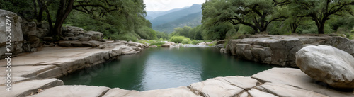 Natural stone pool surrounded by trees and mountains in a lush green valley.