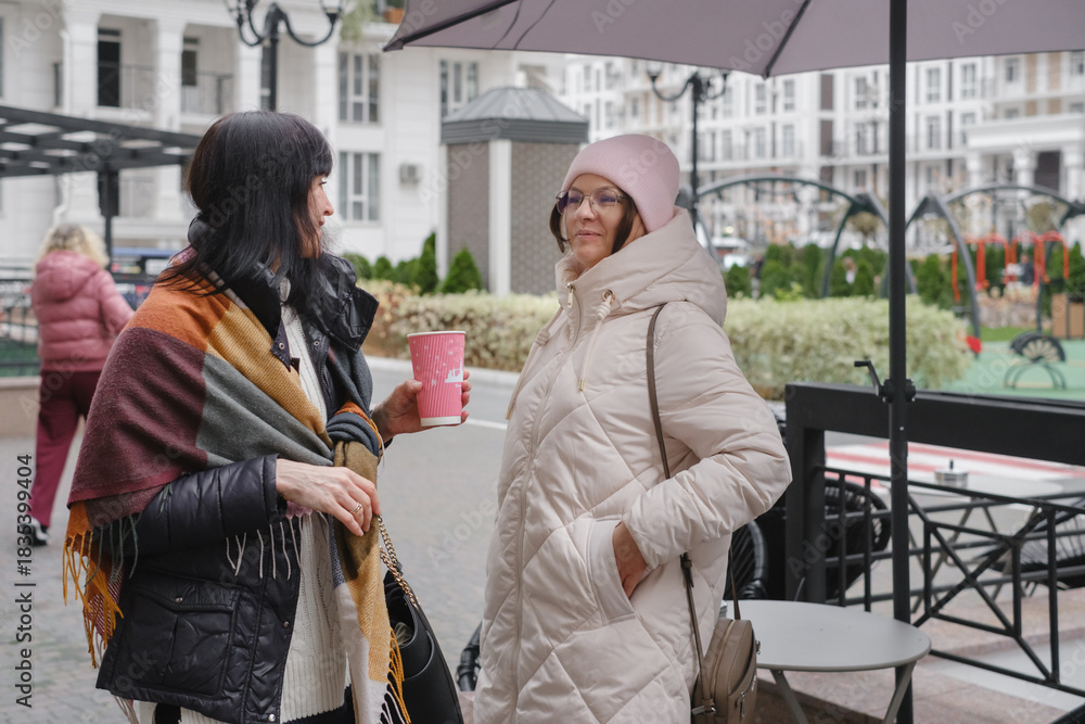 Obraz premium Happy multigenerational female friends enjoy outdoor meetup, checking smartphones and capturing memories with playful selfie on cold day