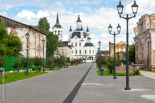 Fototapeta Naklejka Na Ścianę i Meble -  A street in a recreation park in a small Siberian town, bathed in autumn sunshine. At the end of the street is a church. Tourism in Russia