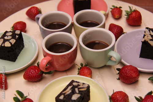 Close-up high-angle shot of espresso cups with rich brownies topped with almonds, surrounded by fresh strawberries. A warm, inviting dessert and coffee scene perfect for cafés and food branding.