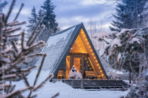Winter vacation in a wonderful house by the forest. A woman drinks hot chocolate or coffee in winter in a house near the forest on the eve of Christmas or New year.