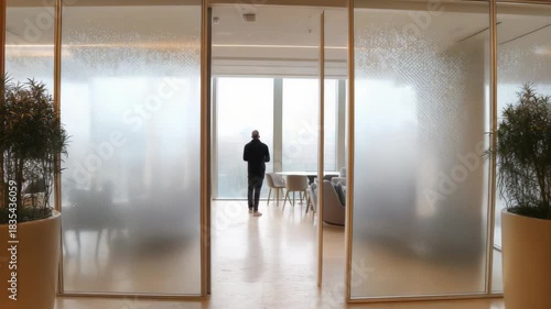 Man walking through modern office doorway with frosted glass and plants