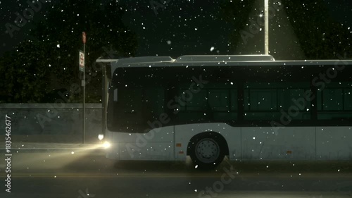 A white and black bus drives on a street at night during a gentle snowfall, illuminated by its headlights and a streetlamp.