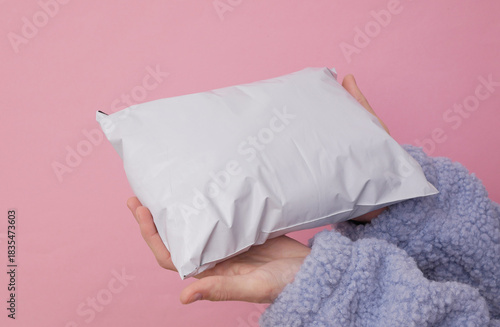 Female hand holding Empty blank white plastic parcel bag. Shipping Plastic Postal Packing Mockup on pink background