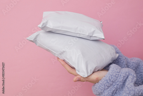 Female hand holding Empty blank white plastic parcel bags. Shipping Plastic Postal Packings Mockup on pink background