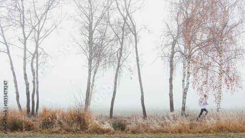 Man, runner in leggings and hoodie is running on footpath in frosty, fog Czech landscape. Sport, active healthy lifestyle background