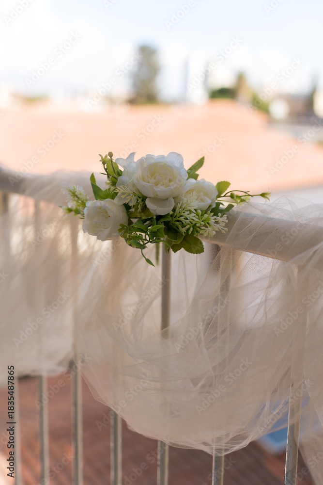 Fototapeta premium Decoration with white flowers on a railing at an outdoor venue in bright sunlight during a wedding ceremony setup