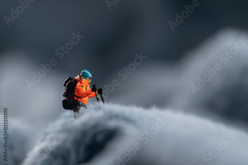 A miniature mountain climber figurine on a fuzzy fleece lining resembling a snow-covered surface, with a blurred background of a mountain or ice wall