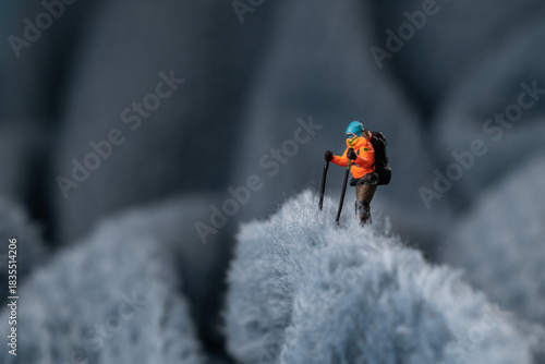 A miniature mountain climber figurine on a fuzzy fleece lining resembling a snow-covered surface, with a blurred background of a mountain or ice wall