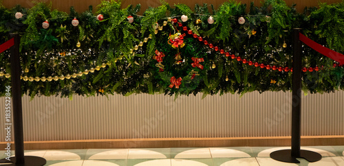 A beautifully decorated Christmas tree stands in the center of an elegant hotel lobby, surrounded by wrapped gifts, festive ornaments, and warm ambient lighting. The scene includes a modern reception 