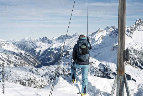 Ski tourer enjoying the summit view in the snowy Alps near Warth, Tyrol, during a bright winter adventure.
