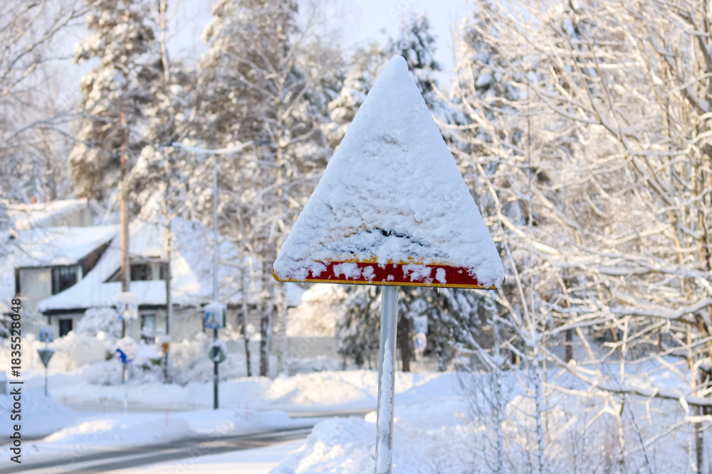 Fototapeta premium Road sign covered in snow. It has snowed so much that the road signs are partially covered. A typical winter landscape in a small Finnish town. Sunny February day.