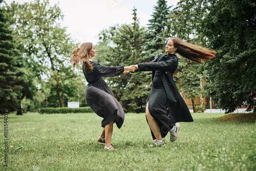 Two young women spinning and holding hands in green park