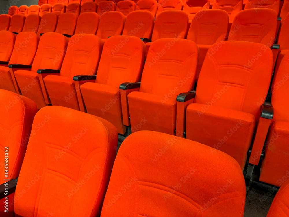 Fototapeta premium The rhythmic arrangement of the red fabric event hall chairs in their empty state.