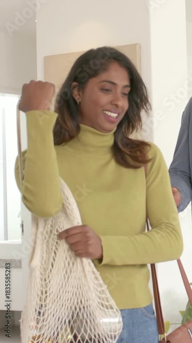 Vertical video: Returning couple handing white mesh grocery bag in entryway after shopping