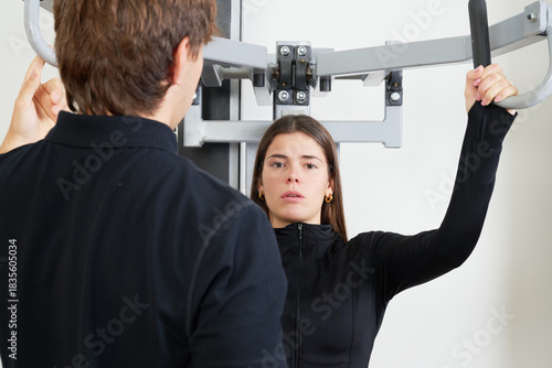 Personal trainer guiding young woman during gym workout