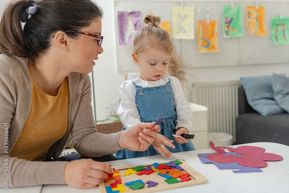 Fototapeta premium Caregiver and young girl engaging in a learning activity with colorful wooden blocks in a bright preschool classroom