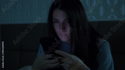 A young woman checks her phone in a dark room at night, illuminated by the screens cold light. A cinematic moment symbolizing anxiety, insomnia, stress, and emotional tension. 