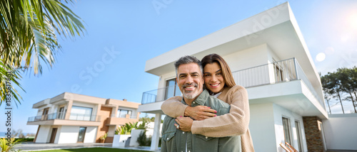 Happy smiling mature older family couple new property buyers modern dream luxury villa owners standing outside house, senior middle aged man and woman in love hugging outdoor. Portrait. Banner ads