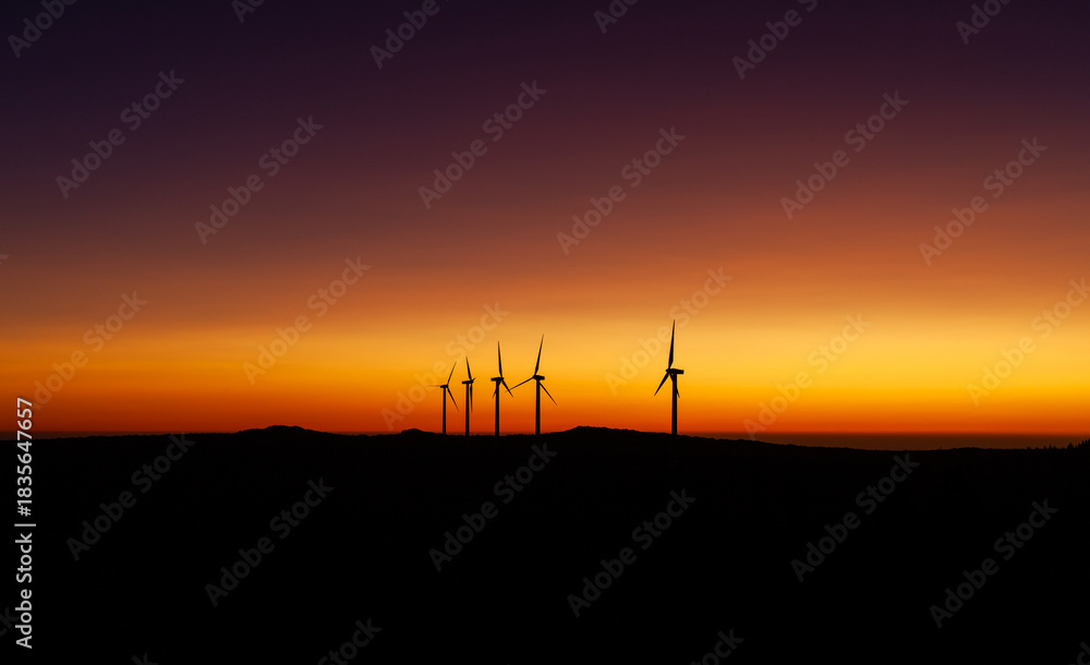 Obraz premium Wind turbines generating green energy at sunset in Madeira, Portugal. Mountain landscape with sustainable technology. Renewable energy in a rural countryside setting.
