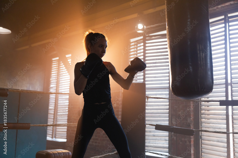 Fototapeta premium Women self defense girl power. Strong woman fighter training punches on boxing ring. Healthy strong girl punching boxing bag. Training day in boxing gym. Strength fit body workout training