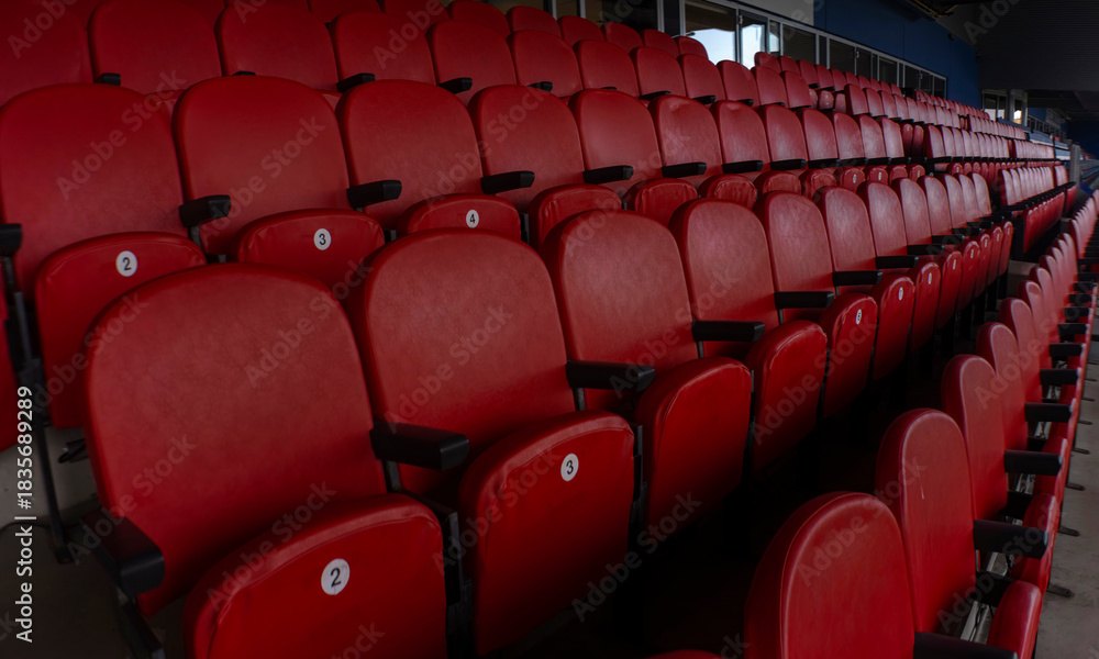 Obraz premium Numbered red stadium seats with angled perspective toward pitch. Shot with anamorphic lens.