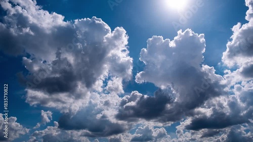 Fluffy white cumulus clouds drift across a vibrant blue sky on a bright sunny day. Sun rays peek through the formations creating a serene and beautiful cloudscape.