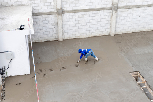Construction worker troweling a fresh concrete floor. Worker using a trowel to finish concrete