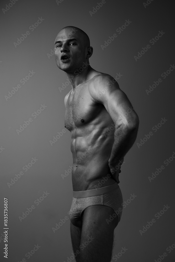 Fototapeta premium Black and white image of a man showcasing strength and confidence, emphasizing muscular physique and expressive pose against a neutral backdrop.