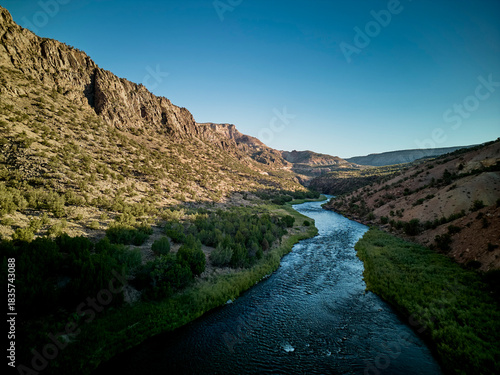River winding through desert canyon landscape with rocky cliffs and green vegetation under clear blue sky