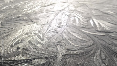sunlight shining on a frozen surface of ice revealing beautiful pretty floral flowery patterns of  freezing water particles forming crystals.  The camera slowly pulls away and zooms out graduallly