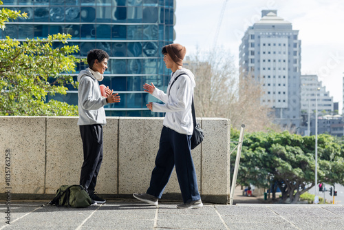 Diverse male friends exchanging football while carrying backpack and headphones on urban terrace
