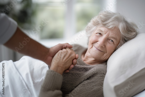 Elderly Woman Lying in Bed Holding Hands with Visitor in Tender Moment.