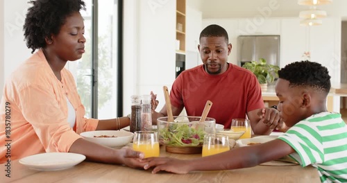 Sitting at kitchen table, African American family praying while giving thanks before eating cereal