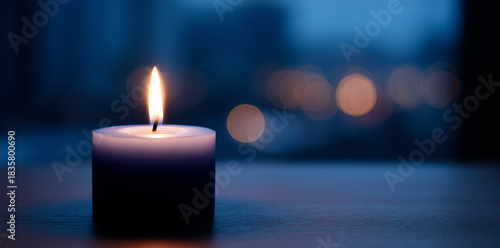 Burning candle with soft flame against a blurred background of lights