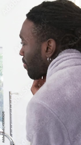Vertical video: Entering bathroom to groom, man in bathrobe using shaver, applying cream