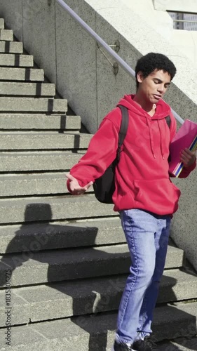 Vertical video: Approaching adult hugging student at campus steps, offering smartphone, copy space