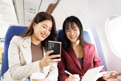 Two women are sitting next to each other on an airplane, both holding cups of coffee. They are smiling and seem to be enjoying each other's company
