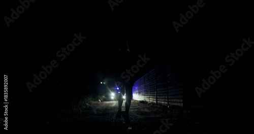 Girl runs from police silhouette in dark alley illuminated by headlights during a tense late-night encounter