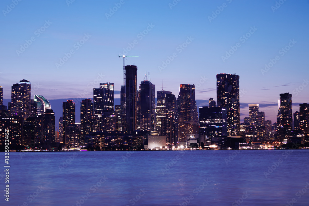 Naklejka premium Toronto skyline at dusk with illuminated city lights reflecting on the water, vibrant urban night view. g.
