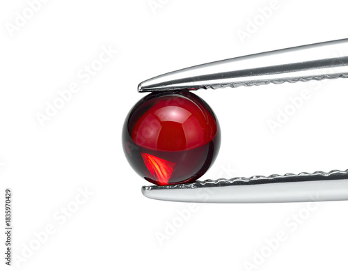 A perfectly round, translucent, garnet-red gemstone held by silver tweezers, set against a black backdrop