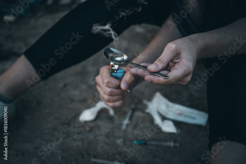 addict makes a shot of heroin. Addiction social problem of modern society. A young woman with drug addiction is sitting with a syringe in a drug den. Close-up of a drug addict's hand with a syringe.  