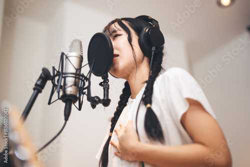 Bild auf Leinwand Asian woman vocalist with a microphone stand wearing headphones record singing s