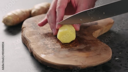 Slow motion man hands slicing fresh ginger root with knife on olive wood board