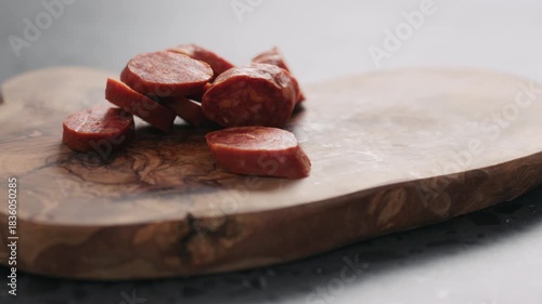 Slow motion man put chorizo slices on olive wood board closeup