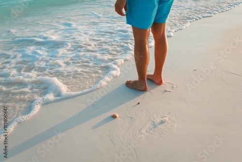 Person in blue shorts standing at the edge of the ocean waves on a sandy beach