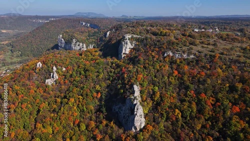 Aerial perspective of Cirque du fer a cheval in France featuring rugged limestone cliffs rising above dense autumn forest and rolling hills, highlighting vivid seasonal colors and dramatic terrain