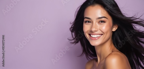 Young woman with long black hair smiles brightly. Her healthy skin glows, makeup subtly enhances her features. She has a radiant complexion and white teeth. This portrait offers copy space for text.