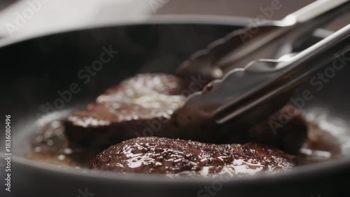 Slow motion man flipping beef steak on nonstick pan with tongs