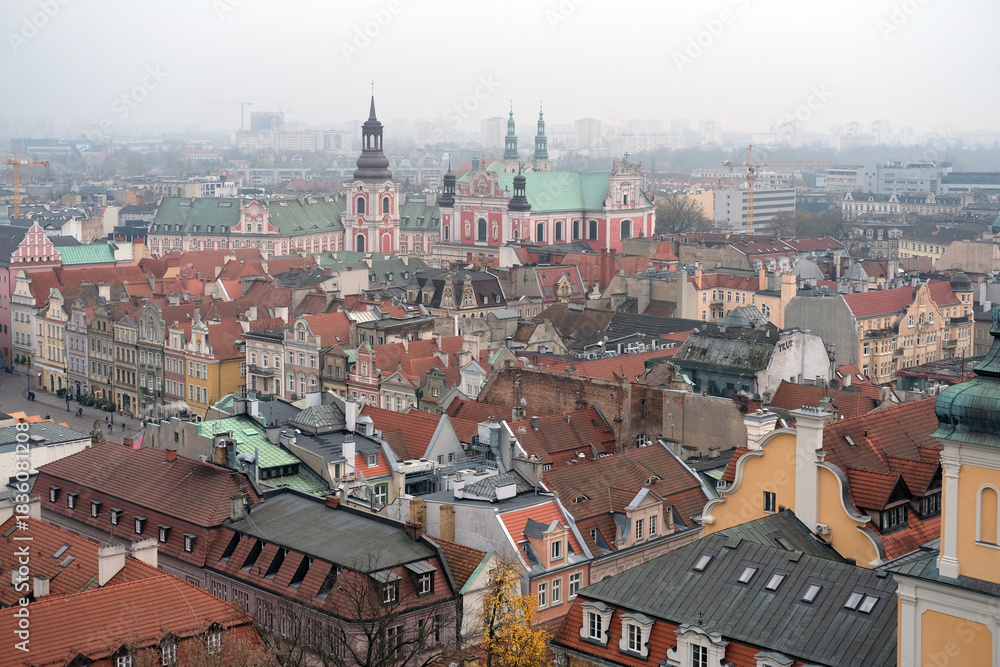 Obraz premium Misty skyline of Poznań featuring ornate church architecture and rows of colorful old town houses.